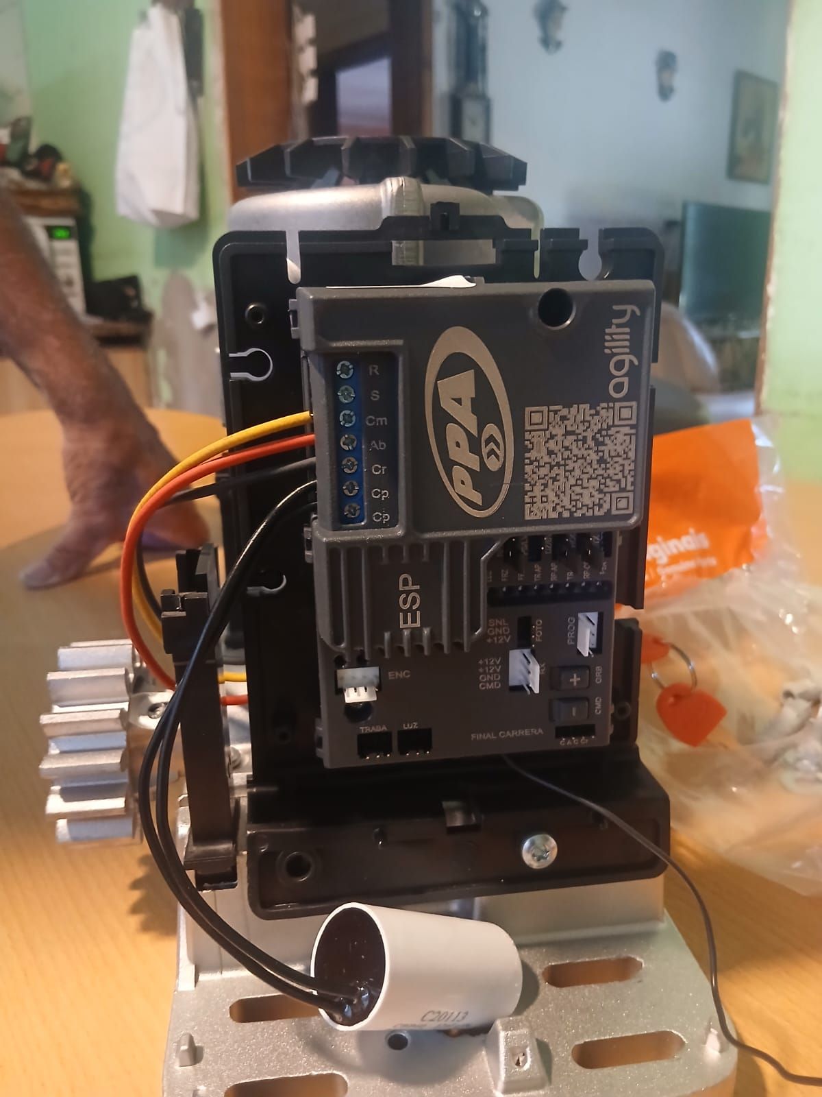 Un motor de apertura de puerta PPA Agility con su placa de control electrónico y condensador, apoyado sobre una mesa.