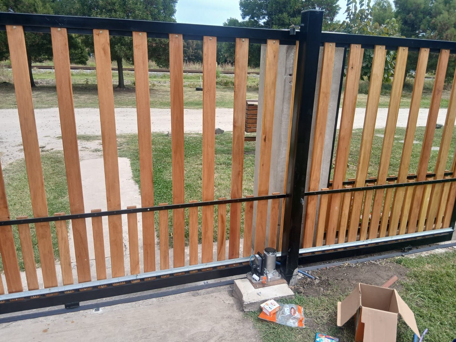 Una puerta corredera con listones verticales de madera clara sobre un marco de metal negro.