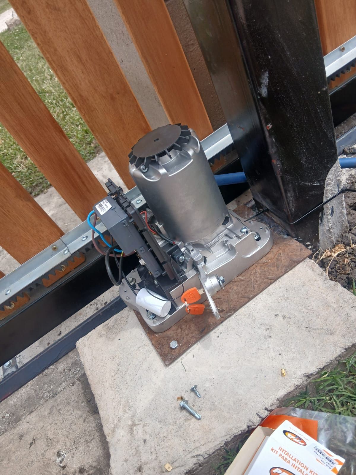 Un motor para puerta corredera montado sobre una base de hormigón, situado junto a una valla de madera.