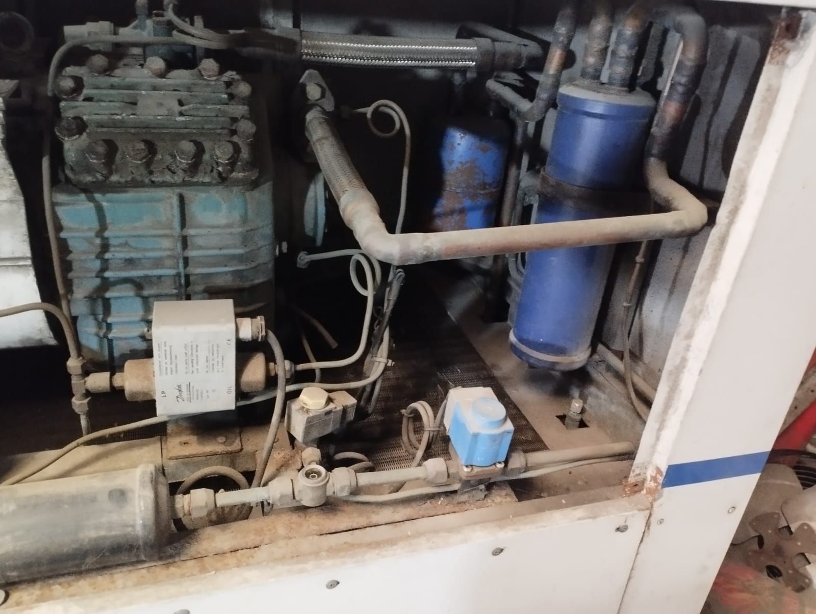 Una unidad compresora de refrigeración industrial con maquinaria azul, tuberías de cobre.
