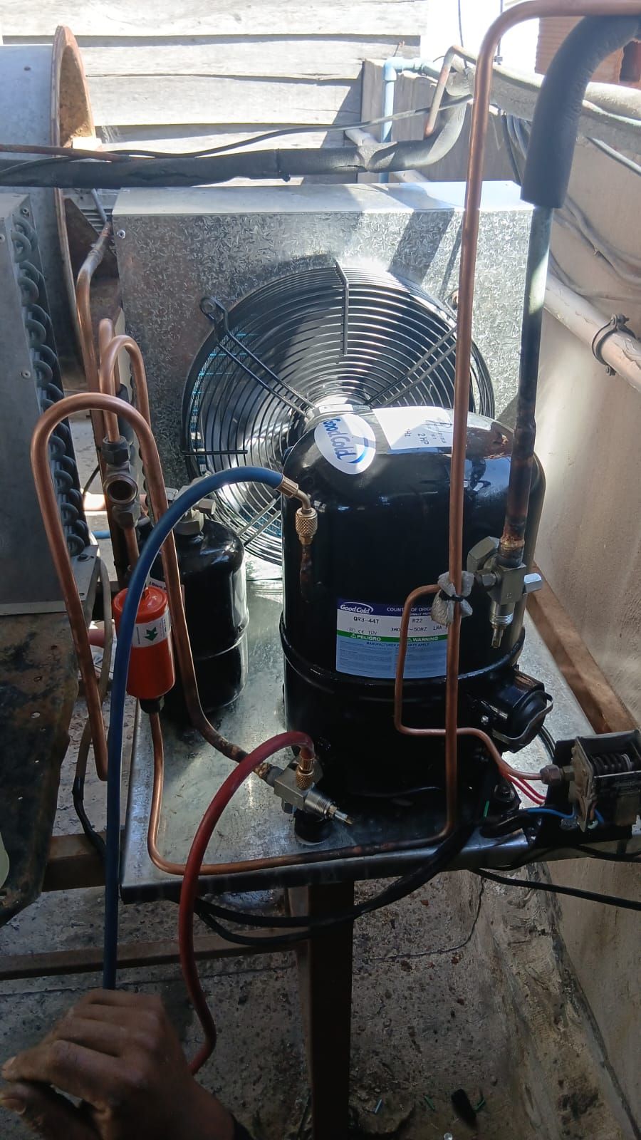 Primer plano de una unidad condensadora de aire acondicionado exterior con compresor, ventilador y conexiones.