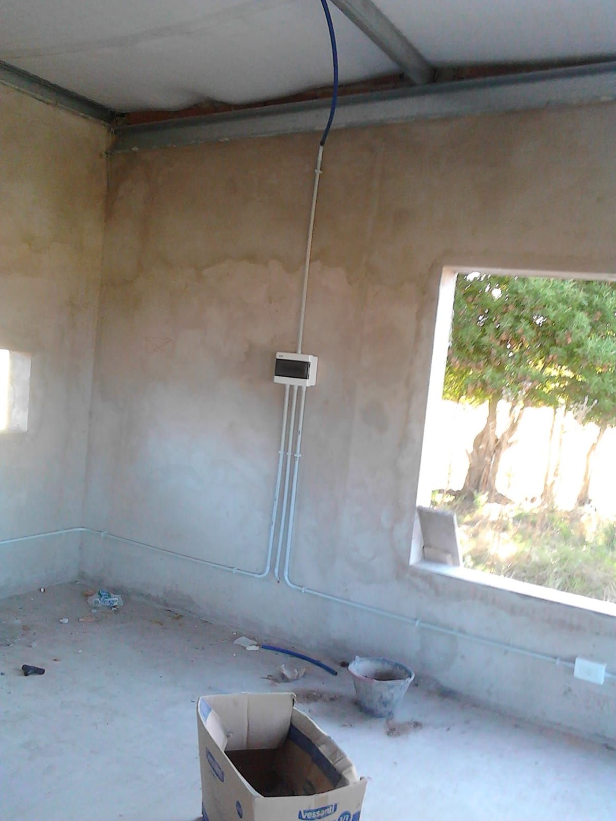 Una habitación sin terminar con paredes de hormigón color beige, una caja eléctrica con tuberías.