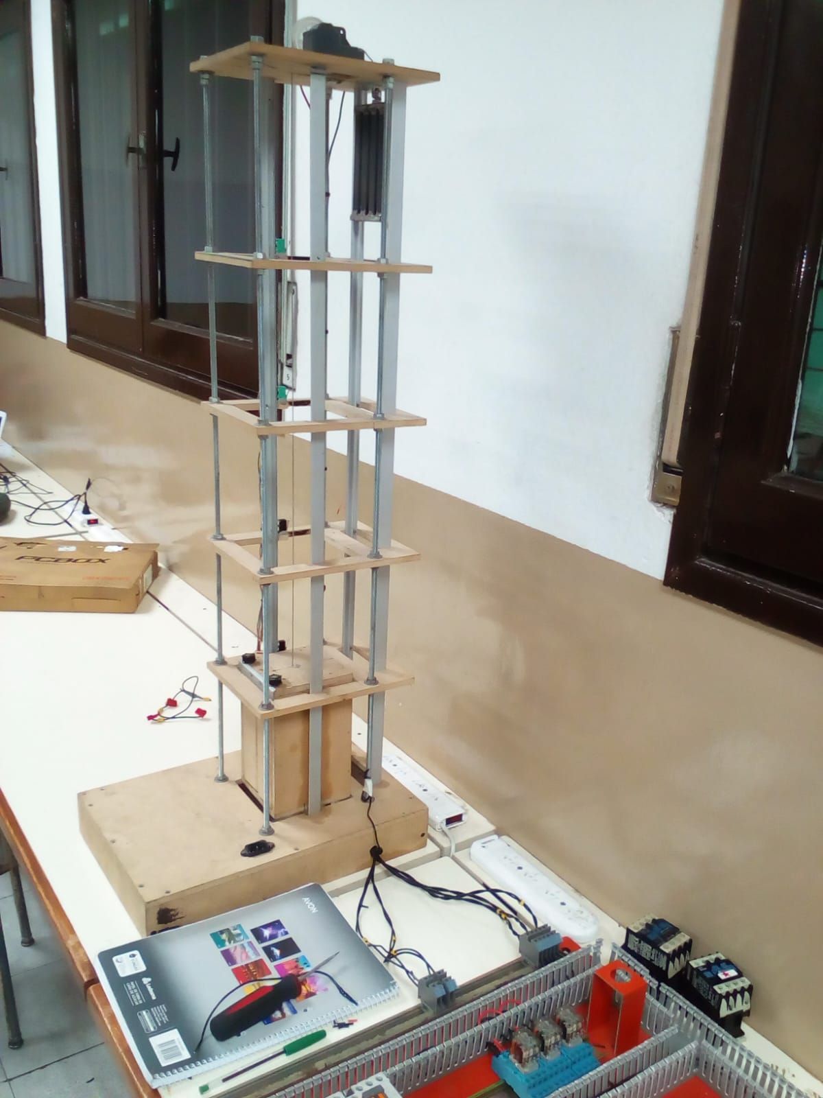 Maqueta de un edificio de varias plantas con mecanismo de ascensor, cables y componentes electrónicos.