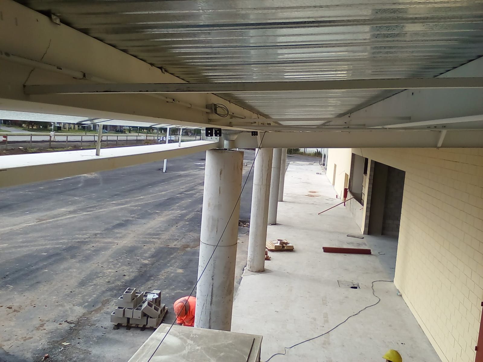 Vista de una pasarela de hormigón bajo un techo metálico, donde se aprecian columnas de soporte.