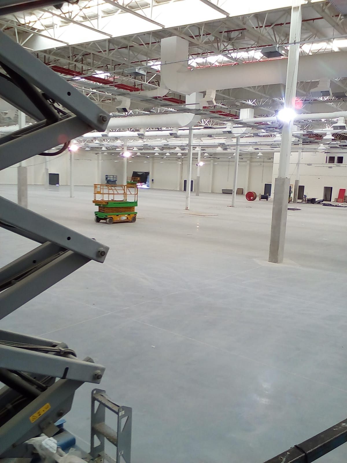 Vista desde una plataforma elevadora de tijera de un gran almacén industrial vacío con suelo de color claro.