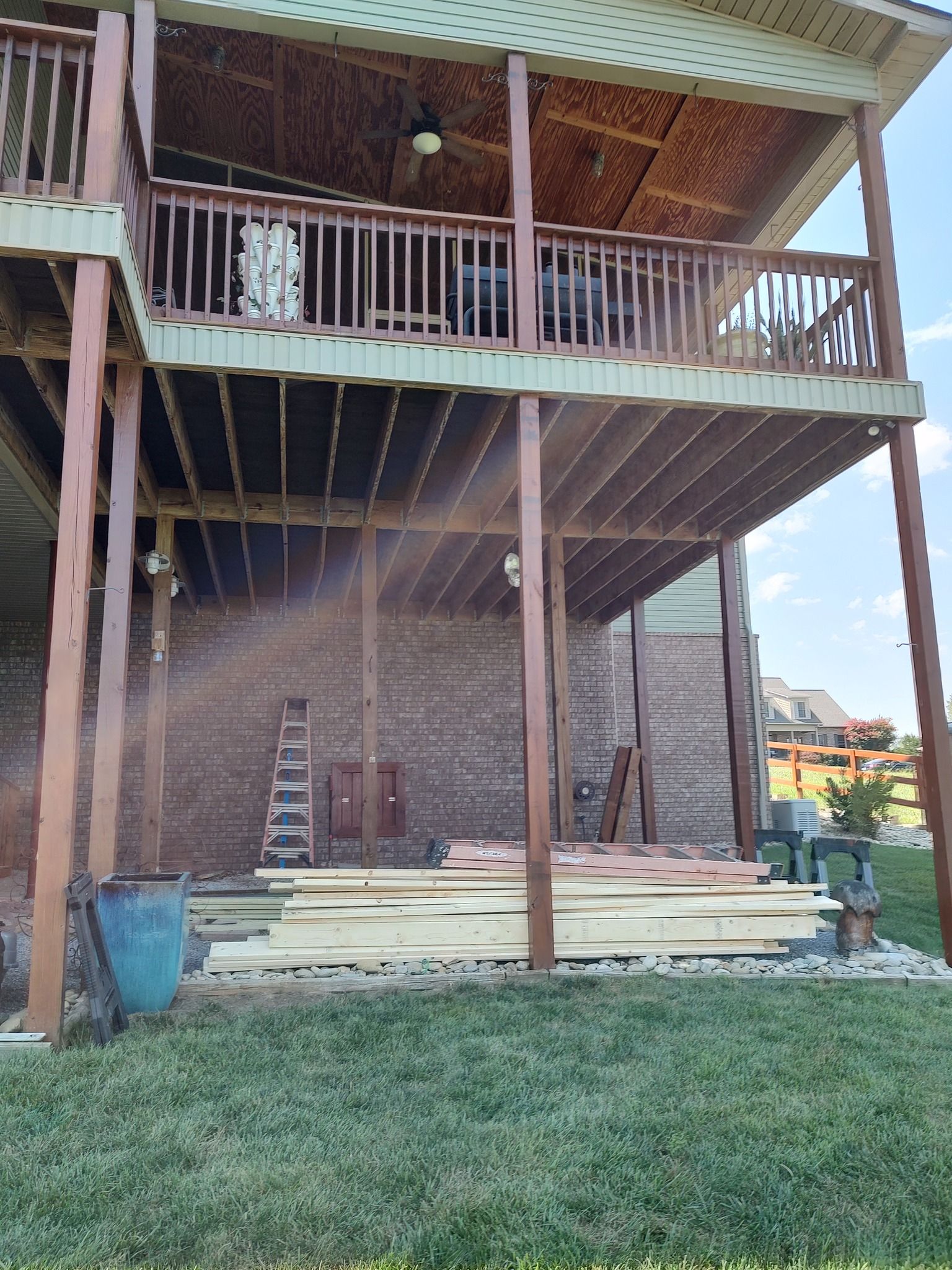 Two-story deck under construction with lumber on the ground and a brick wall.