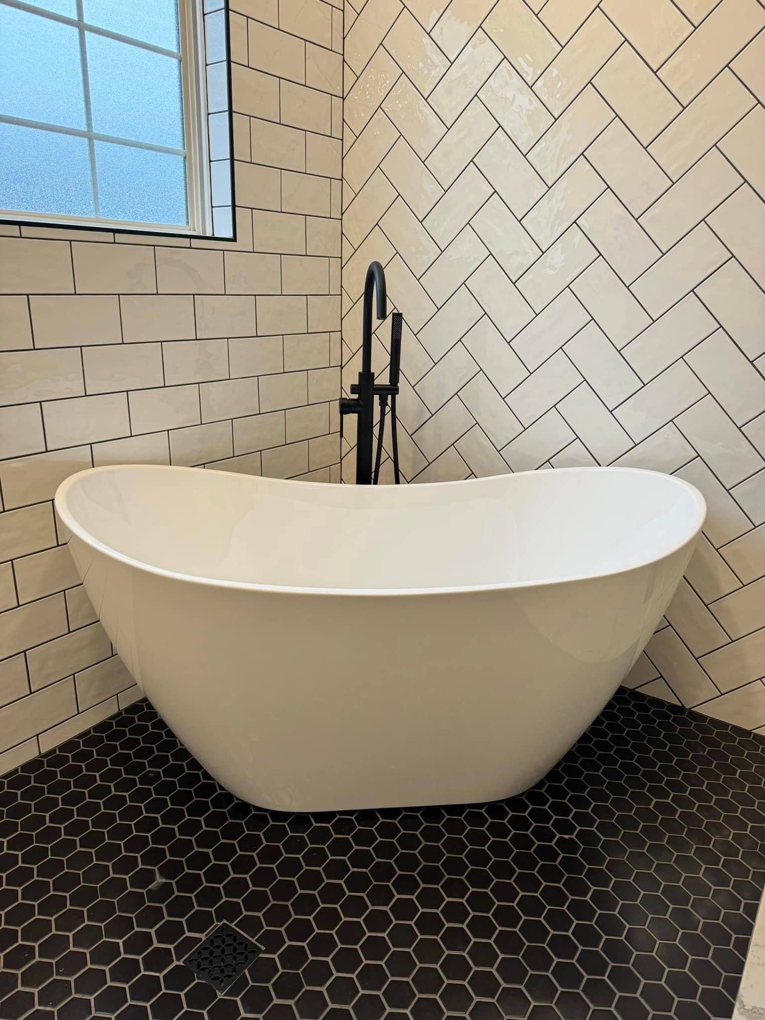 Freestanding white bathtub in corner, black hexagon tile floor, white herringbone tile wall, black faucet.