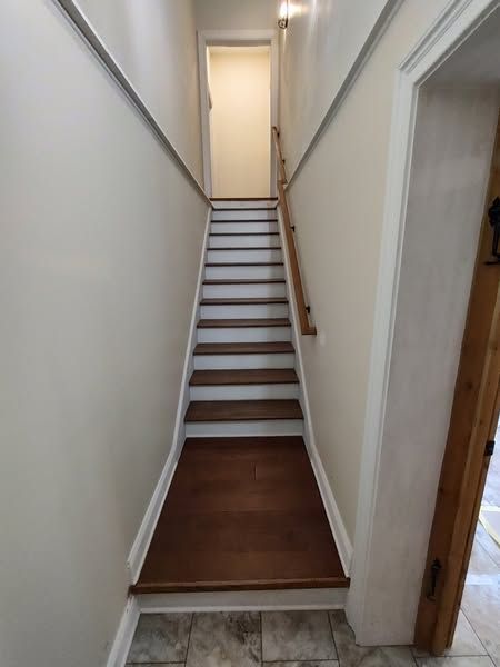 Narrow wooden staircase, brown steps and landing, off-white walls, wooden handrail.