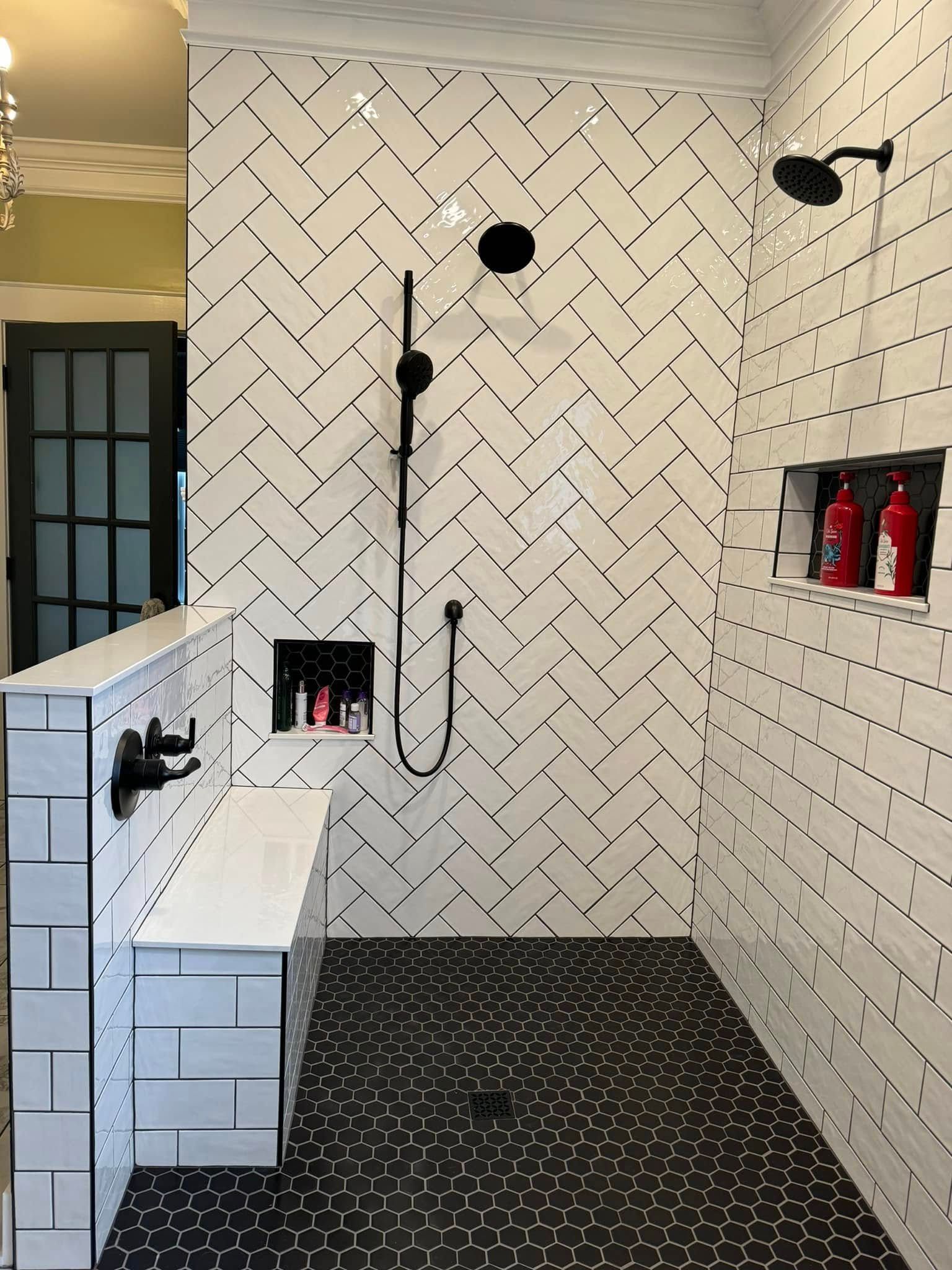 Shower with white herringbone tile walls, black fixtures, black pebble floor, and built-in bench.