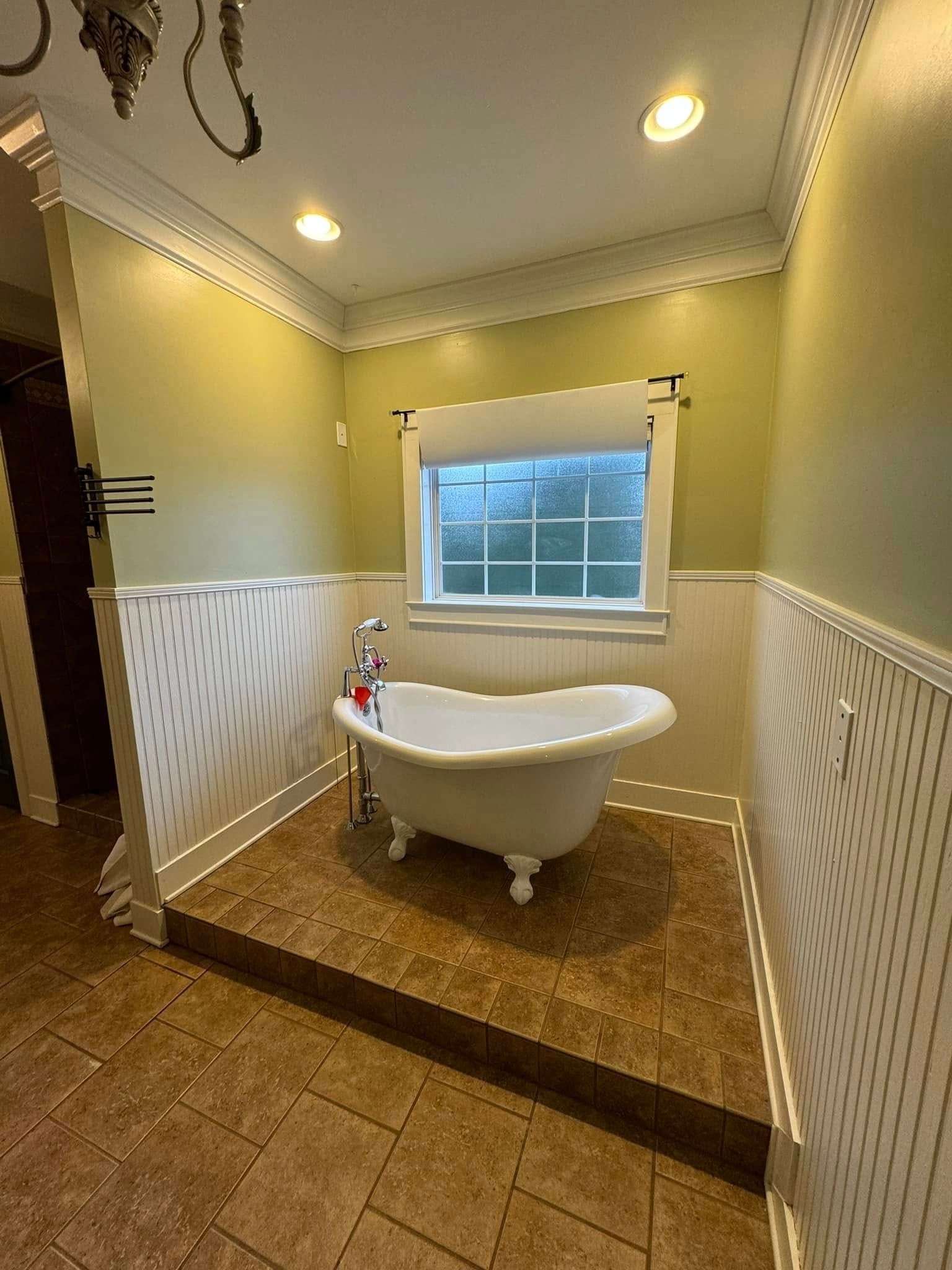 Claw-foot bathtub in a bathroom, with white wainscoting, tile floor, and a window.