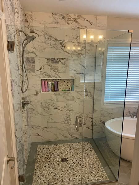 Marble-tiled shower with glass enclosure, a built-in niche, and pebble floor. Includes a bathtub and window.
