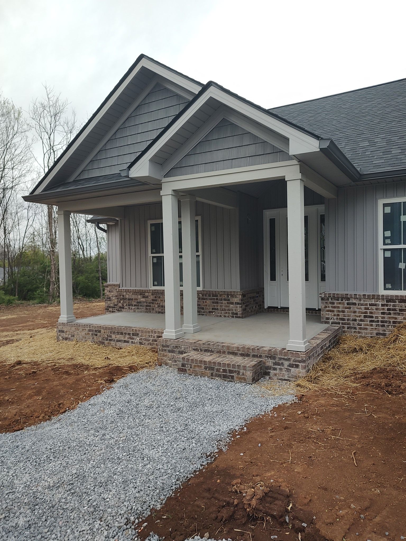 Gray house with a covered porch; gravel pathway leading to the entrance, with brick accents.