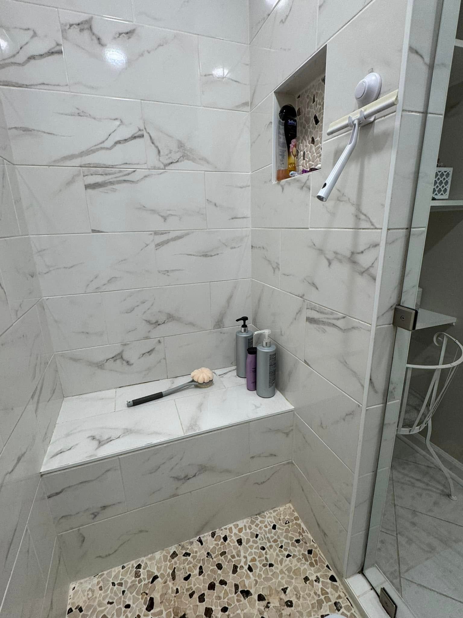 Marble-tiled shower with built-in shelf and niche for toiletries. Glass door on the right.