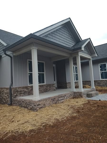 Gray house with a porch. Features brick and white columns, windows, and dark roof.