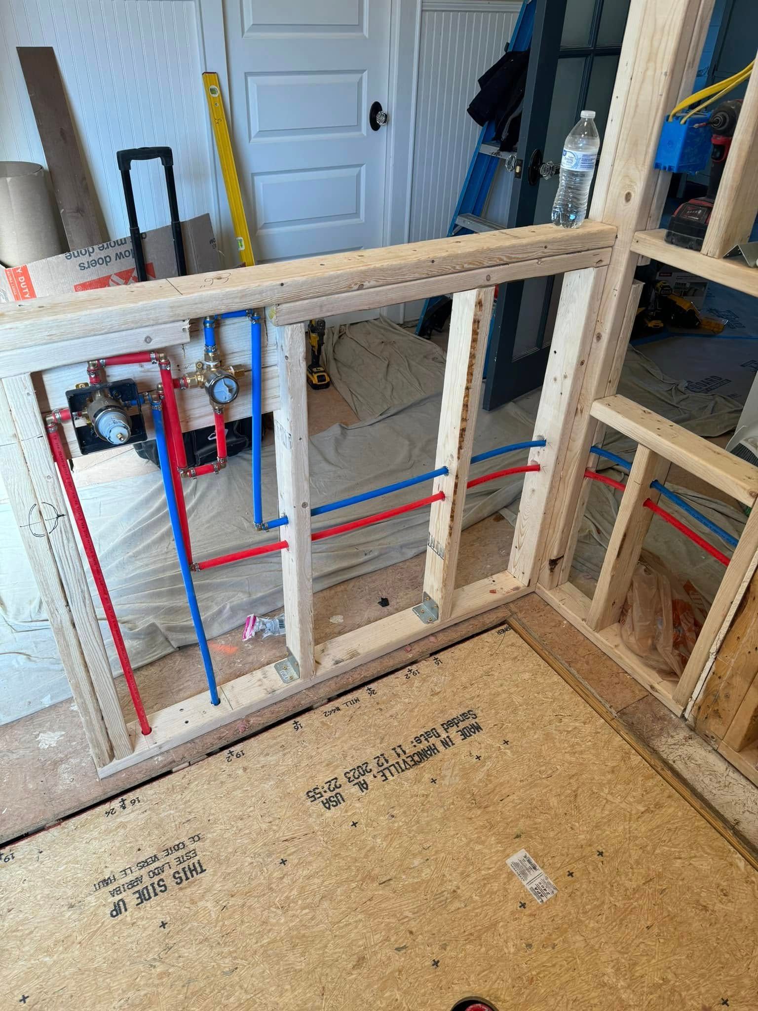 Framed shower plumbing with red/blue pipes, wooden framing, and unfinished construction.