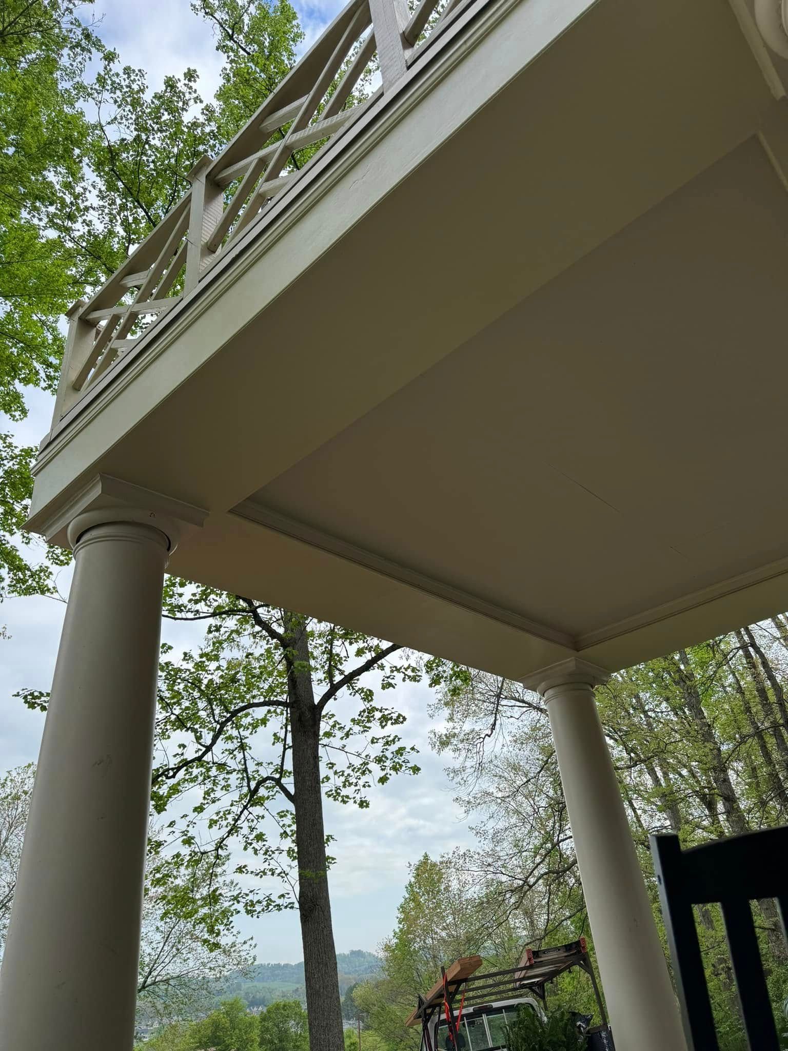 Beige porch supported by pillars, with balustrade above, trees and sky in background.