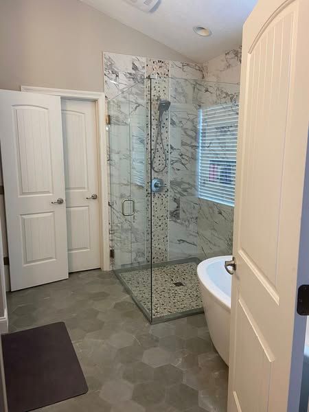 Bathroom with marble shower, tub, white doors, and grey hexagon tile floor.