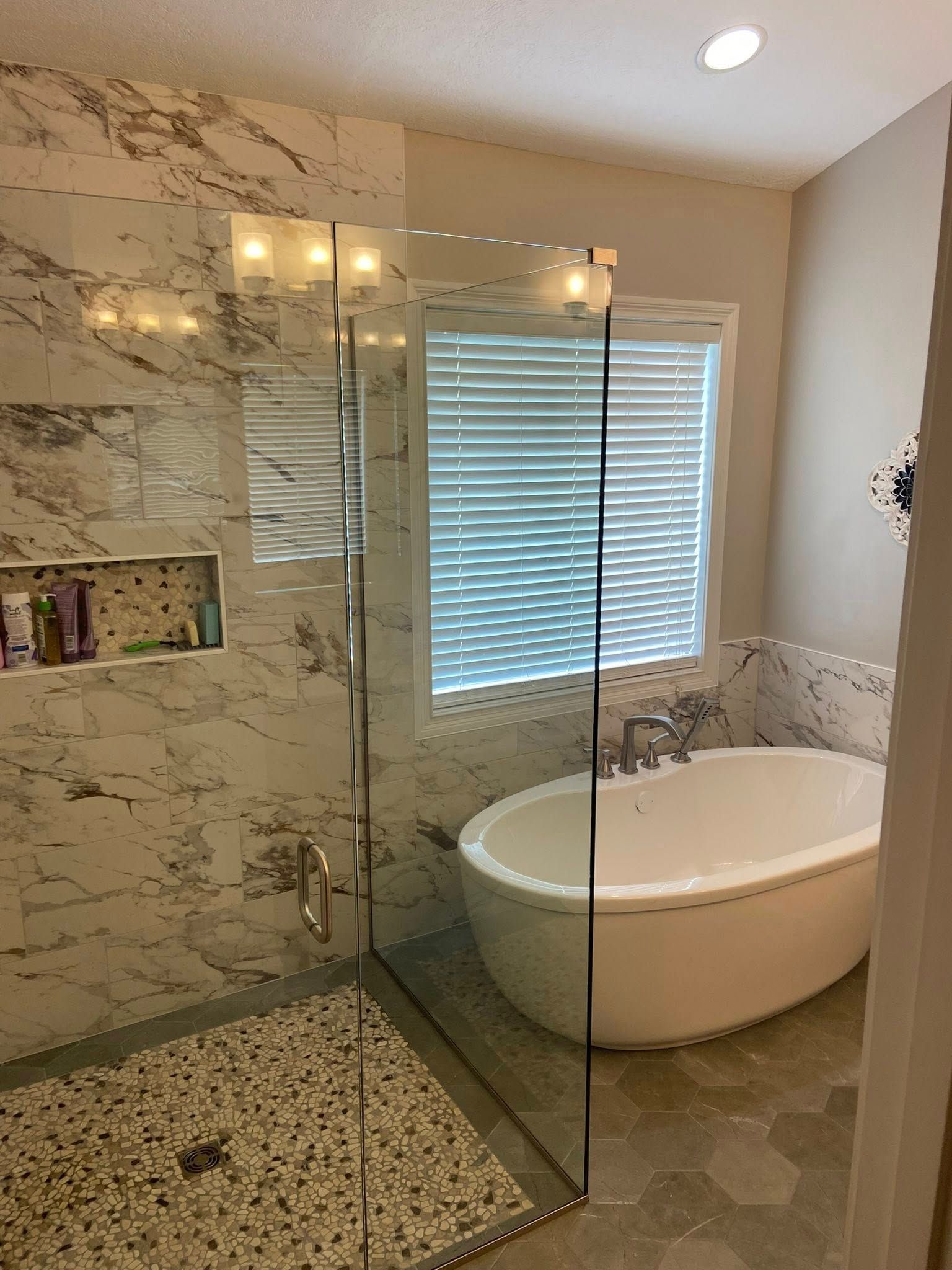 Modern bathroom with a glass shower, freestanding tub, and a window with blinds.