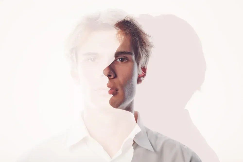Double exposure of a man, semi-transparent; white shirt, looking forward, light background.