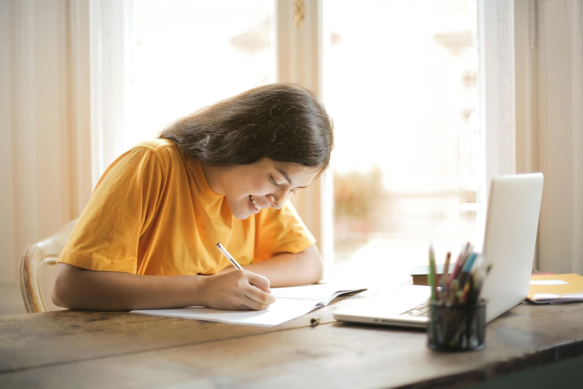 Mulher de blusa amarela estudando e escrevendo em um caderno