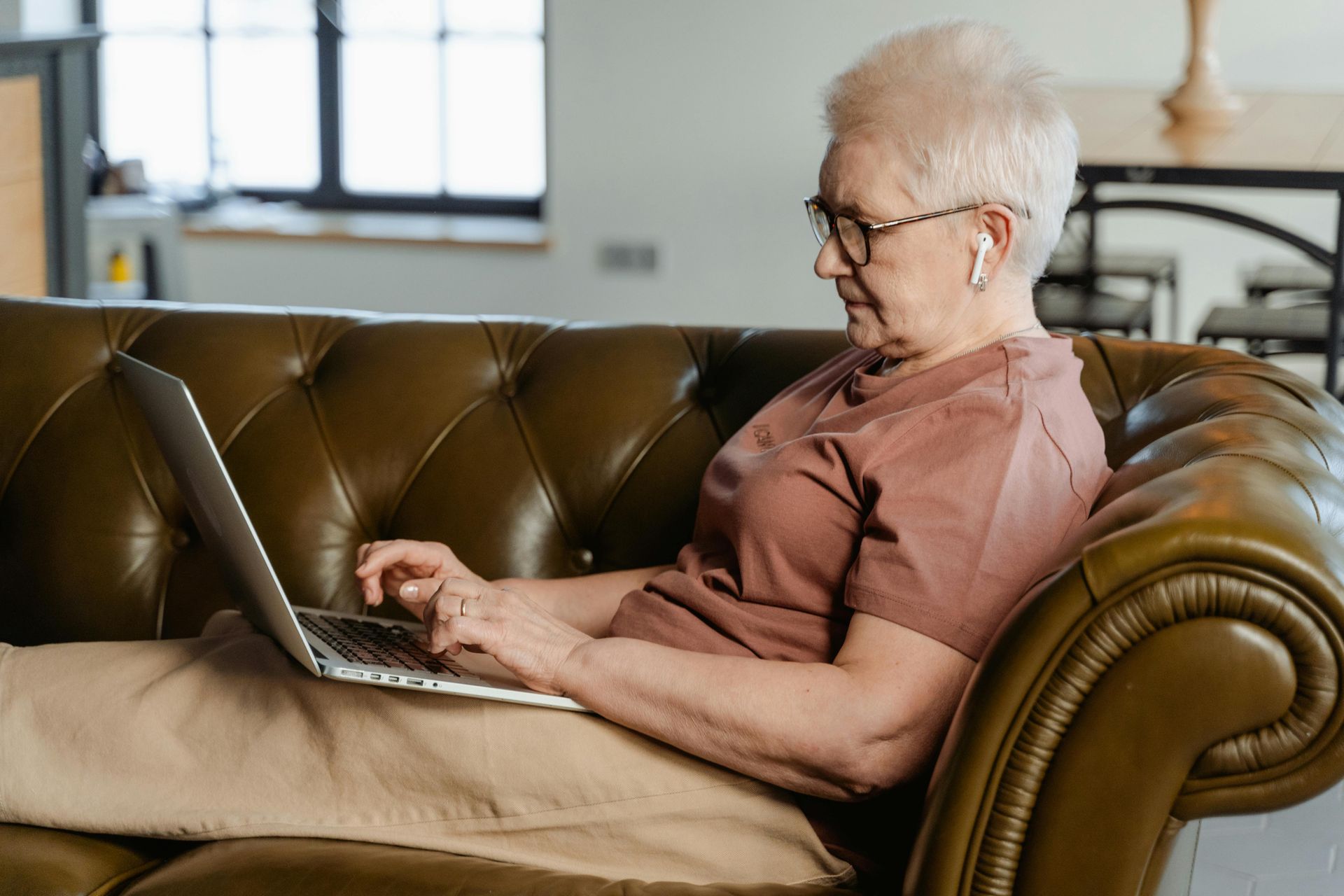 Senhora sentada no sofá com um computador no colo enquanto estuda