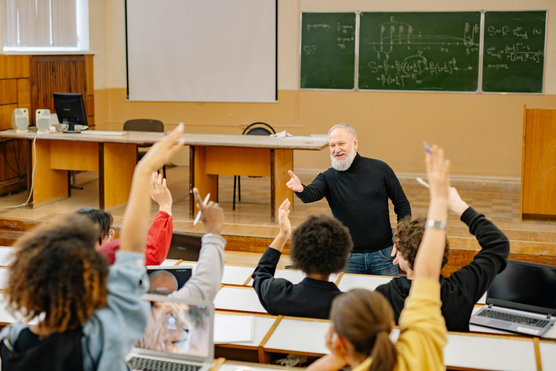 Sala de aula com professor e alunos de braços levantados