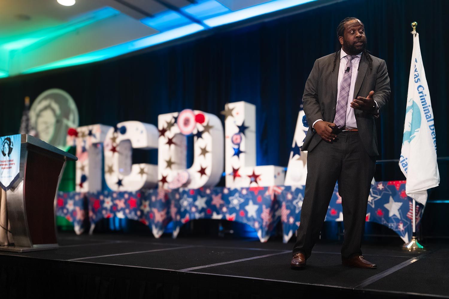 Man with dreadlocks speaks at a podium; banner displays justice figure.