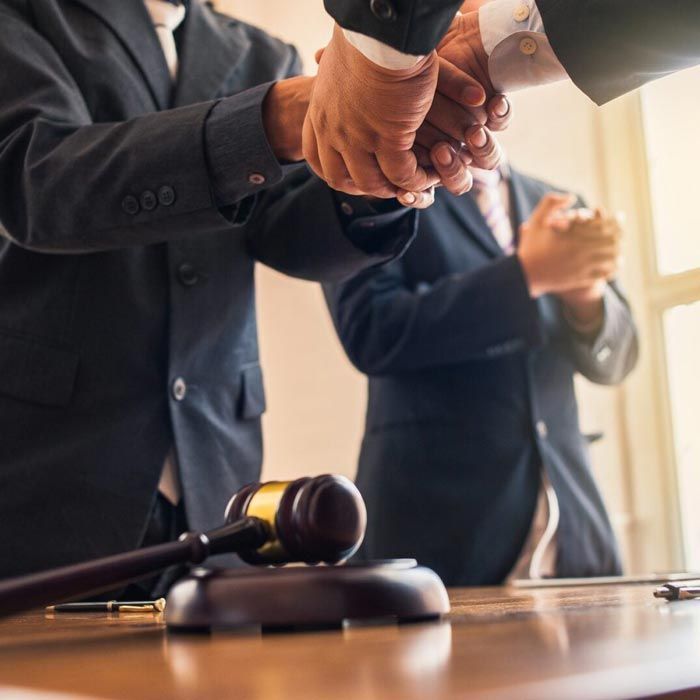 Two men in suits shake hands over a table with a gavel.