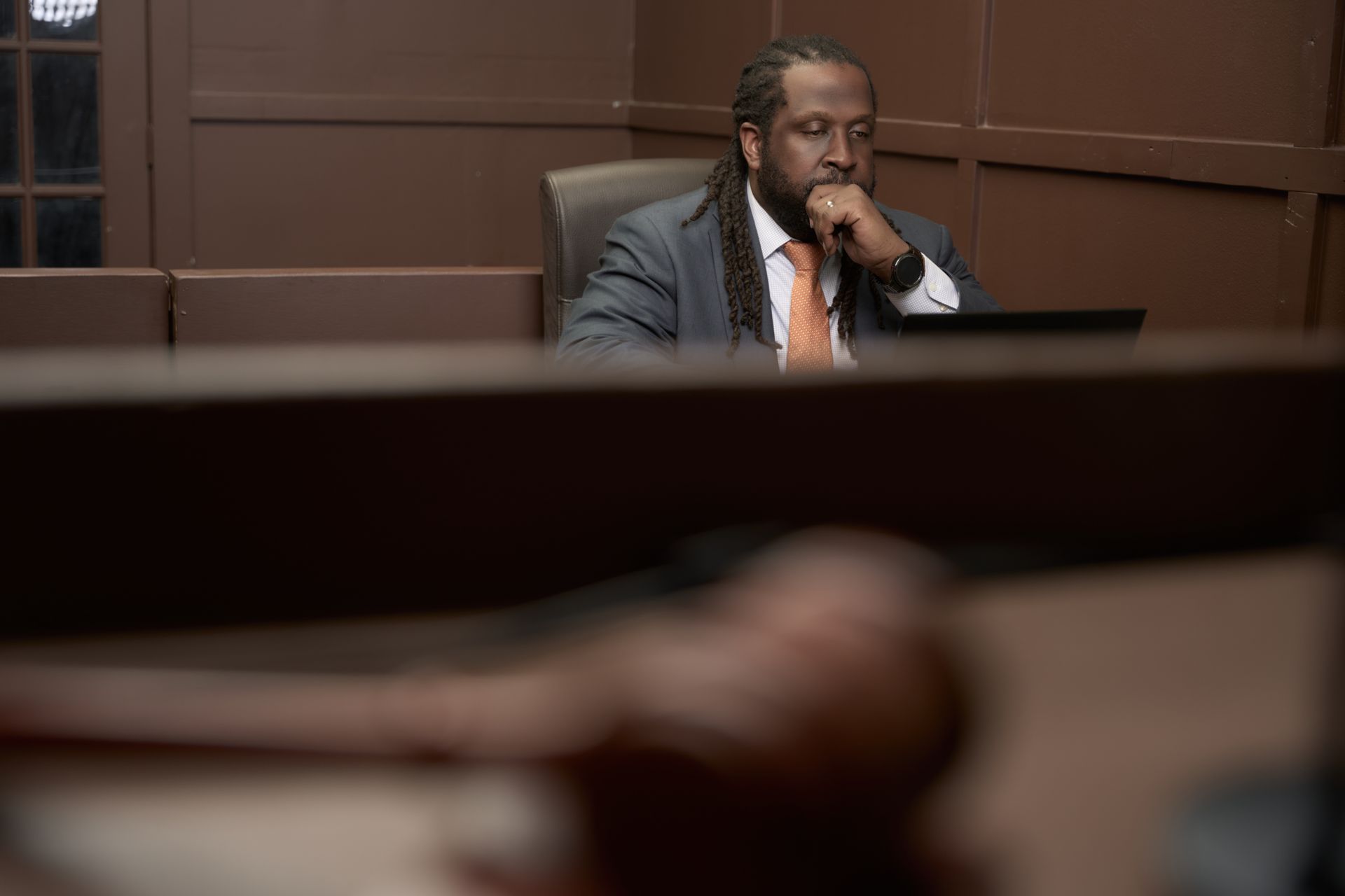 Man in a suit at a table, looking thoughtful, with a gavel in the foreground.