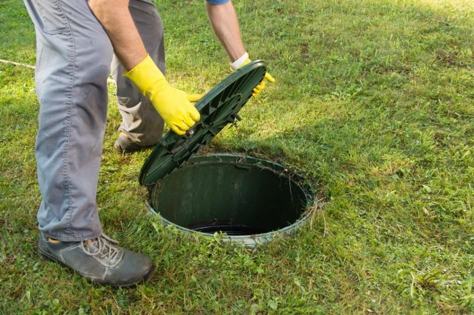 A Man In Yellow Gloves Is Opening The Lid Of A Septic Tank — Liquid Waste Disposal in Port Macquarie, NSW