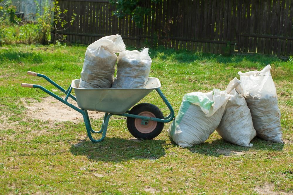A Wheelbarrow Filled With Bags Of Dirt In A Yard — Liquid Waste Disposal in Lake Cathie, NSW