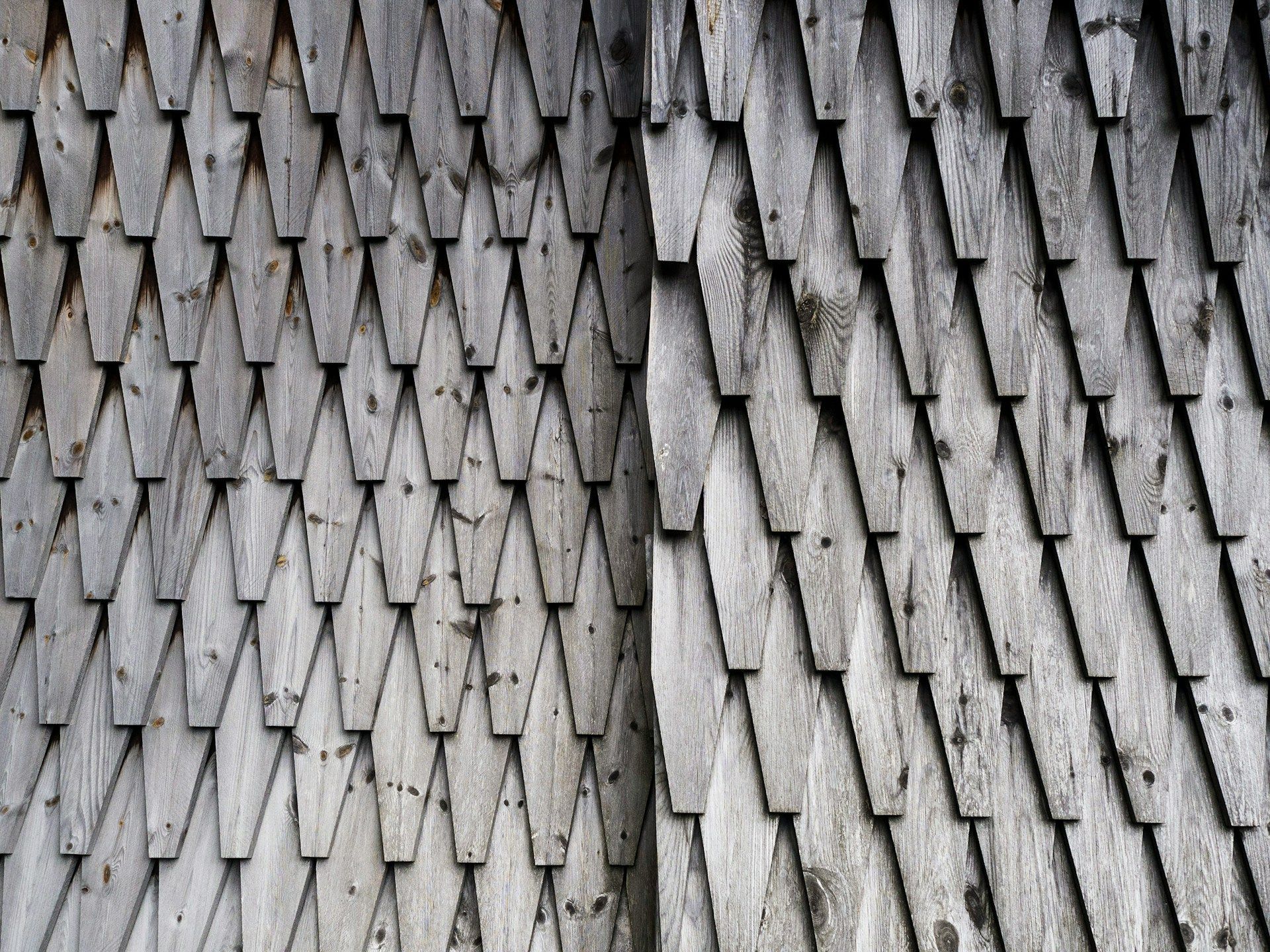 A close up of a wooden wall with a pattern of wooden shingles.