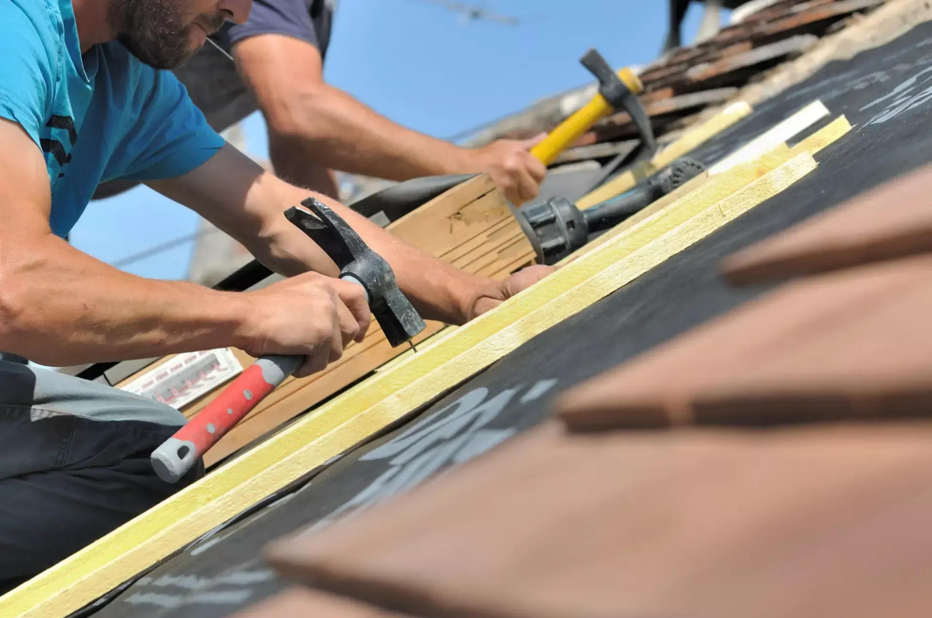 Two men are working on a roof with hammers.