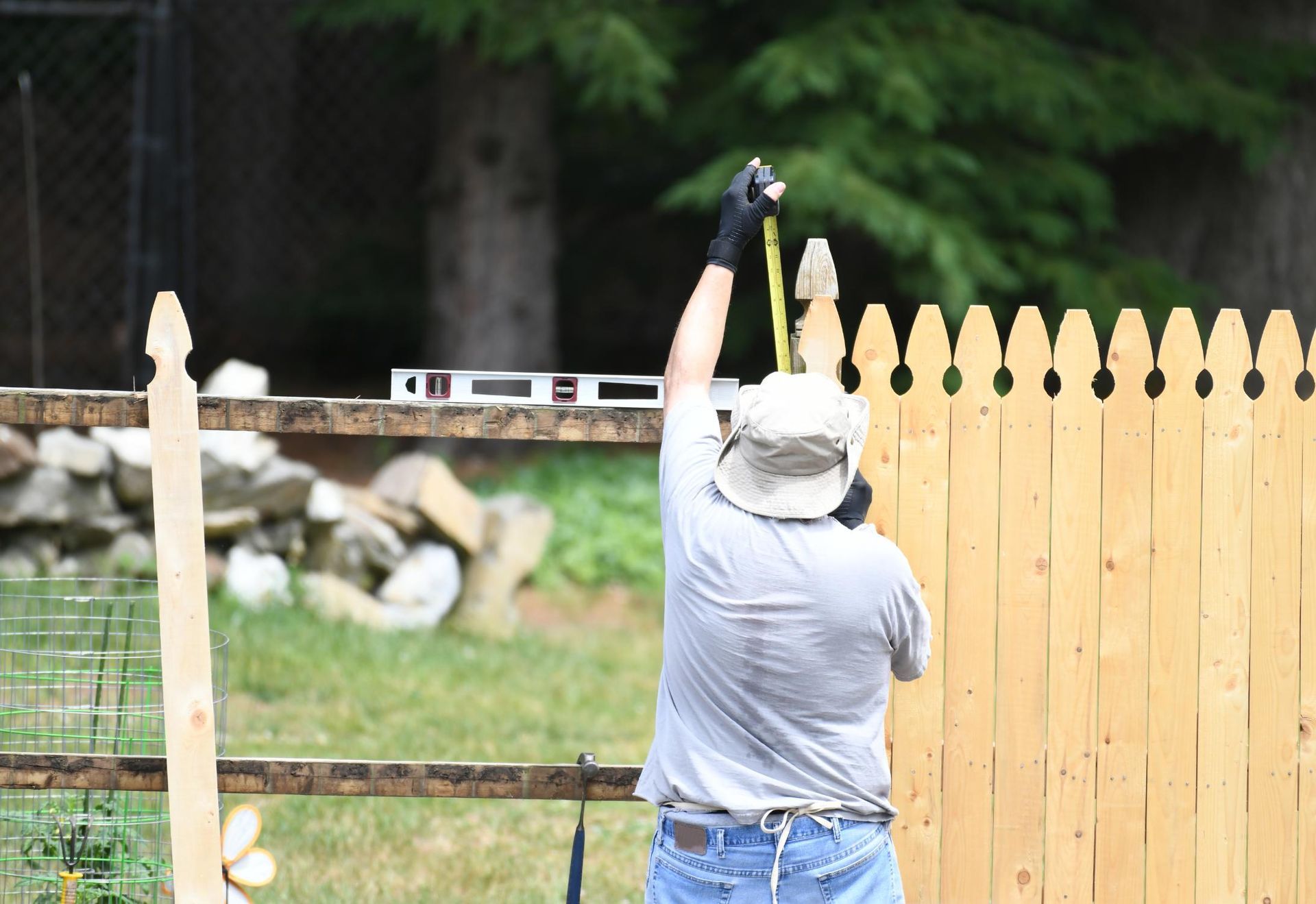 Person measuring a wooden fence outdoors, holding a tape measure high.