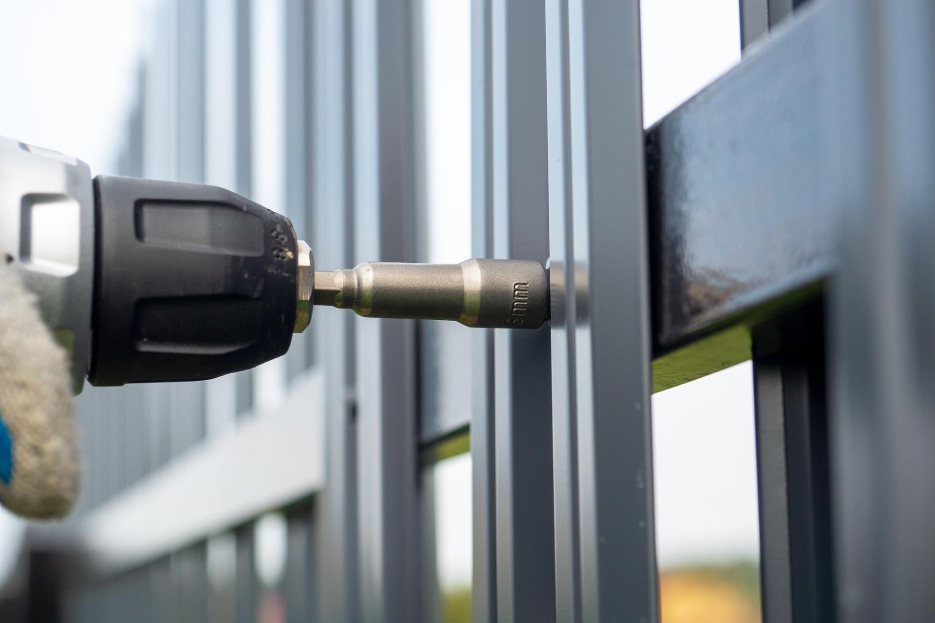 Person using a drill to secure metal fencing, outdoors.