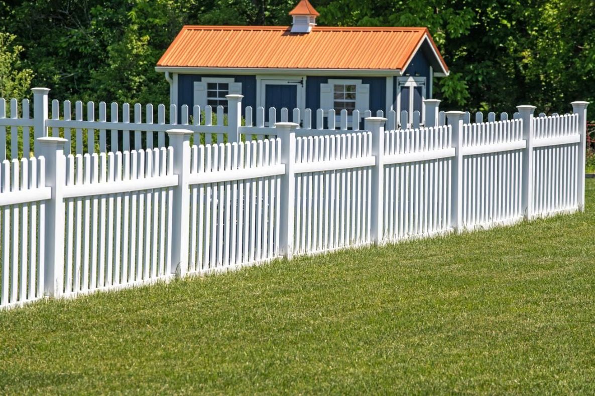 White picket fence surrounding a grassy yard and a blue shed with an orange roof.