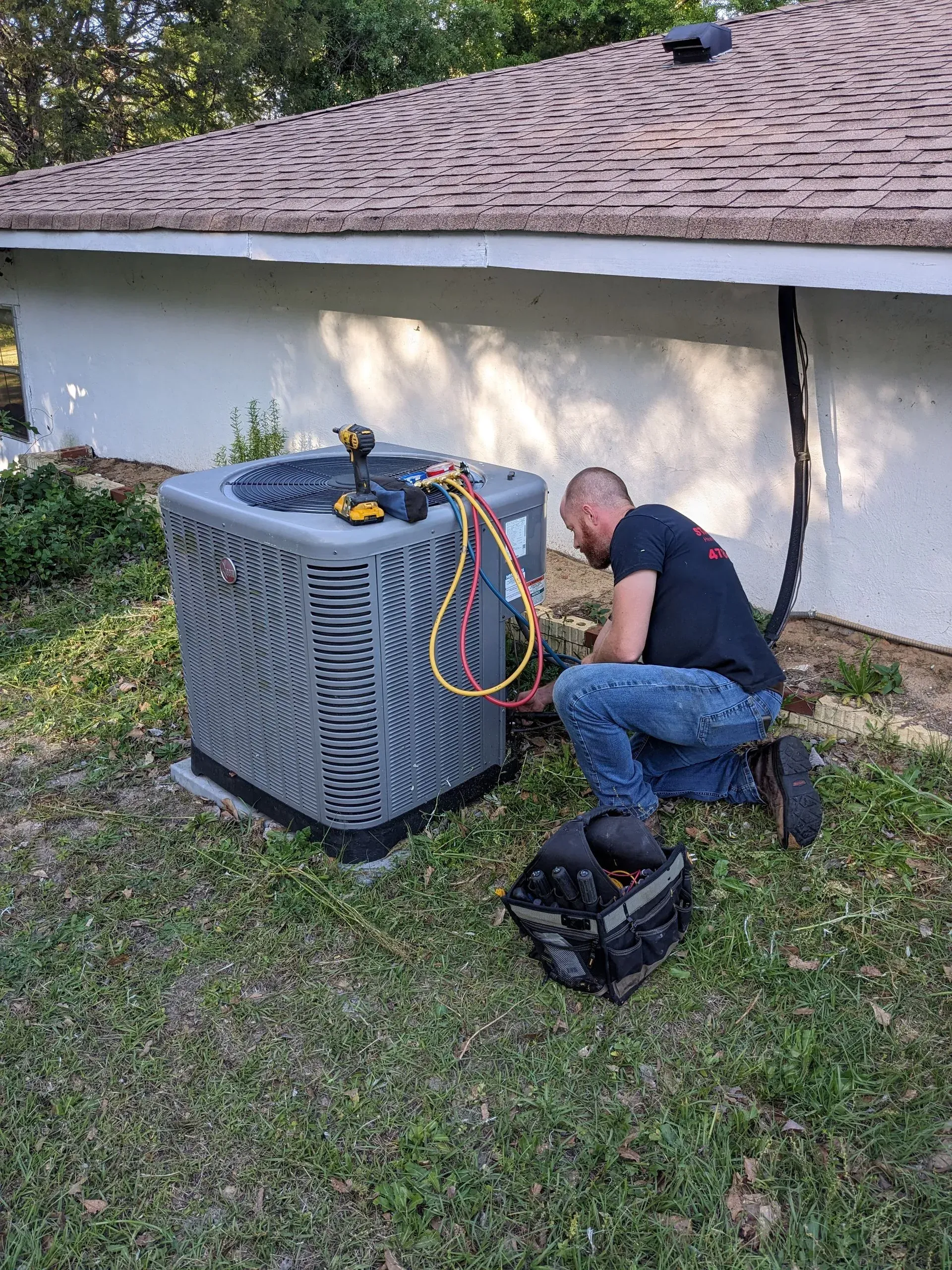 A man is working on an air conditioner outside of a house.