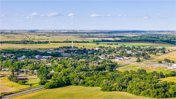 Aerial view of a small town nestled in a green valley, with fields and open plains stretching toward the horizon under a blue sky.