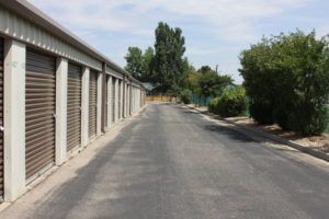 Exterior view of storage units with closed, brown roller doors along a paved drive.