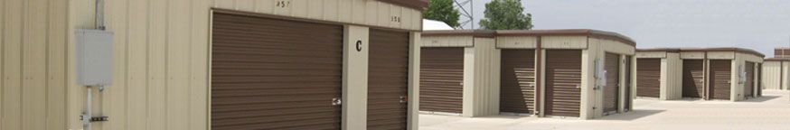 Storage units with brown doors, beige walls, and light-colored ground under a bright sky.
