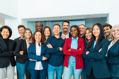 Group of diverse people in business attire smiling with arms crossed, in a bright office space.