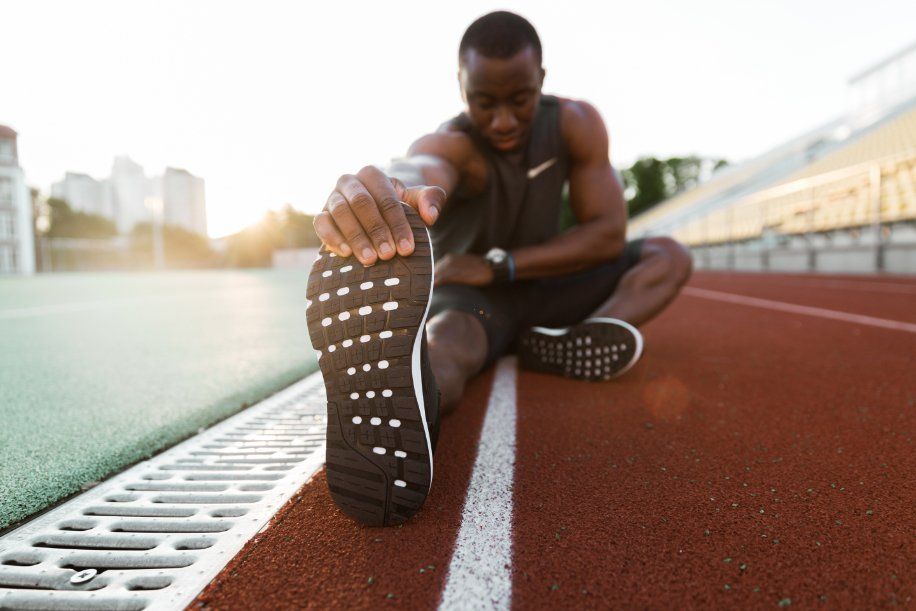A man is sitting on a track stretching his legs.