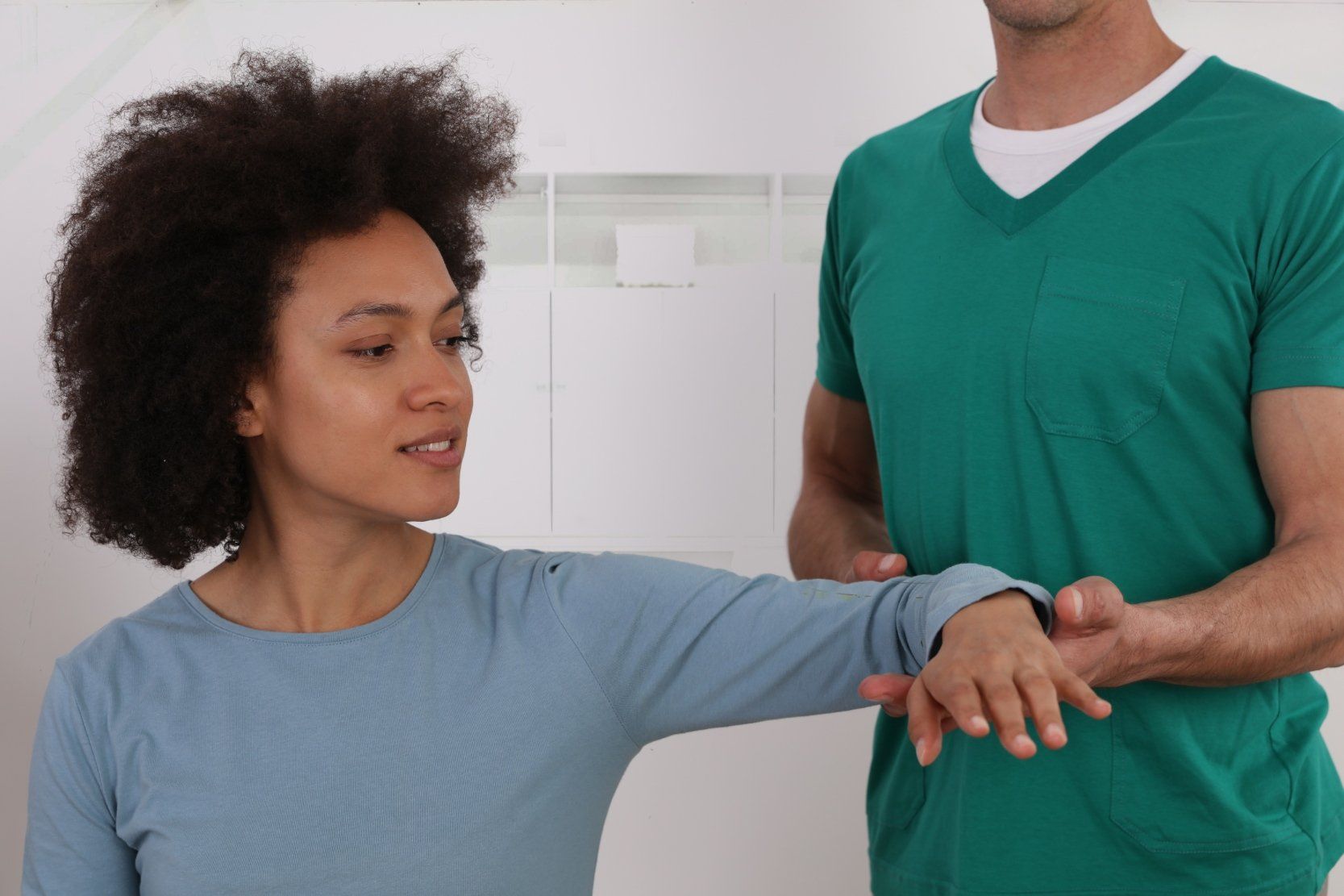 A man in a green shirt is helping a woman stretch her arm.