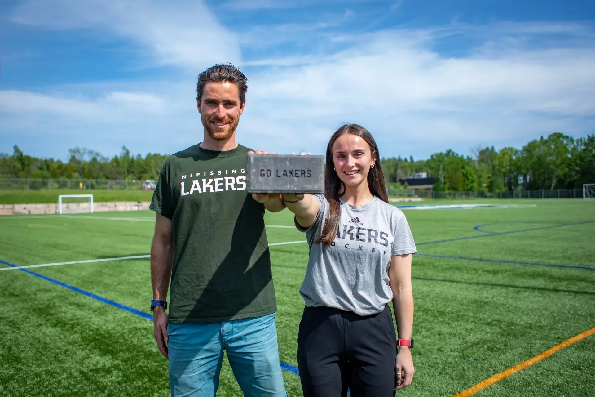 A man and a woman are standing on a soccer field holding a brick.