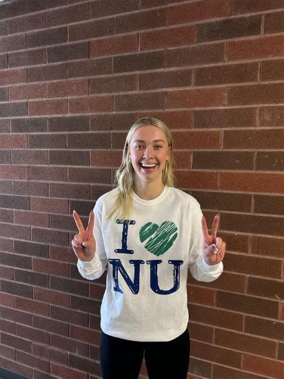 A woman wearing a sweater that says 'i love nu' giving a victory sign