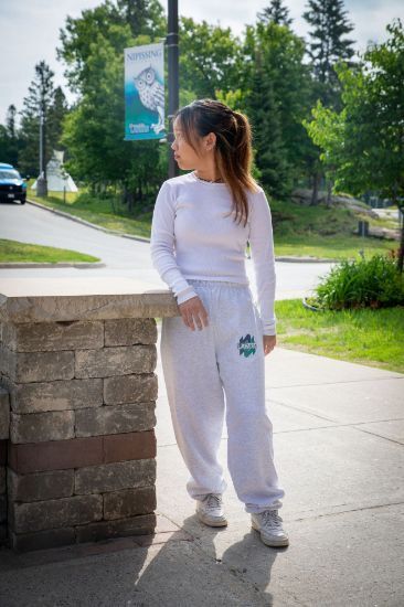 A woman wearing white sweatpants and a white shirt is standing on a sidewalk.