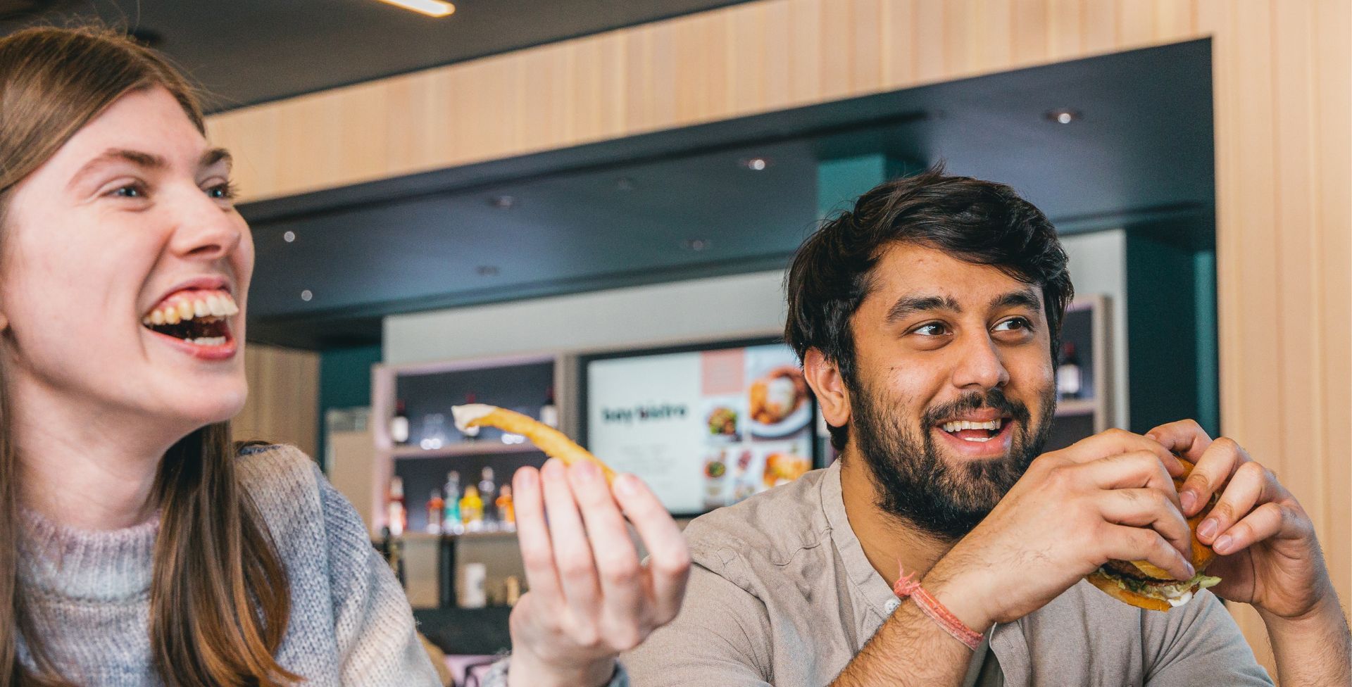 A man and a woman are sitting at a table eating hamburgers and fries.