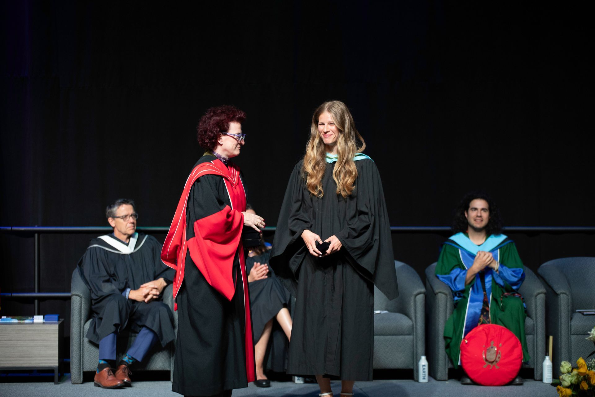 Two women in graduation gowns on a stage.