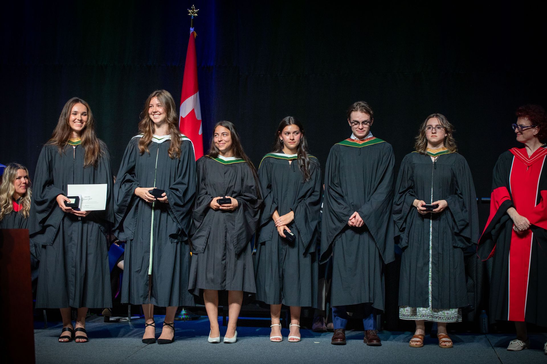 A group of graduates are standing on a stage in front of a Canadian flag.