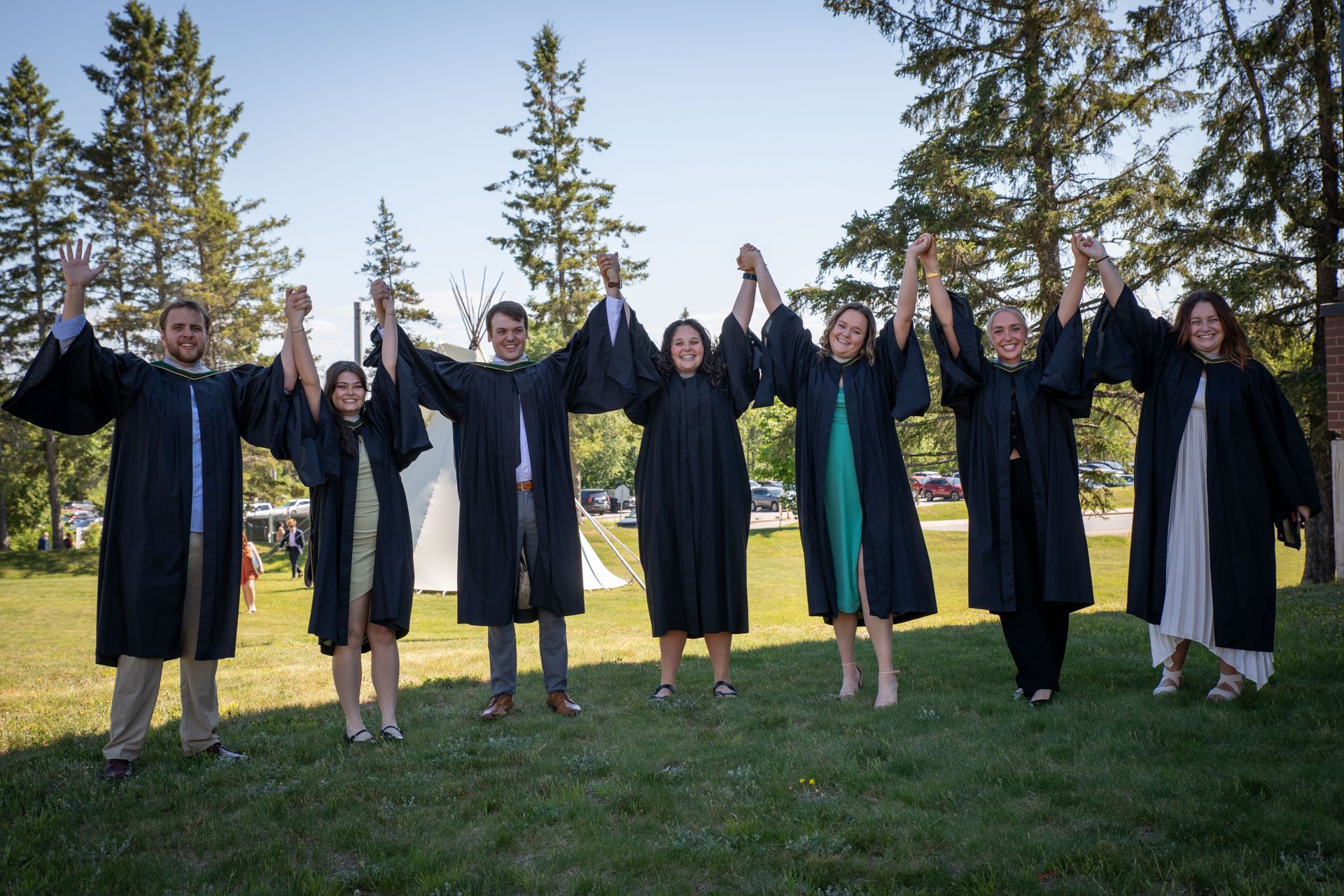 A group of people in graduation gowns are holding hands in a field.